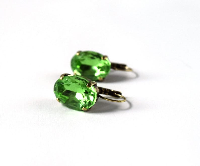 May include: A pair of green oval-shaped earrings with gold-toned metal settings and hooks.