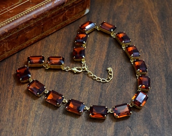 Puede incluir: Un collar de oro con una cadena y piedras preciosas rectangulares de color marrón.