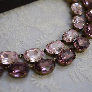 May include: A double-strand necklace with oval-shaped pink and purple rhinestones. The necklace is made of metal and has a vintage look.