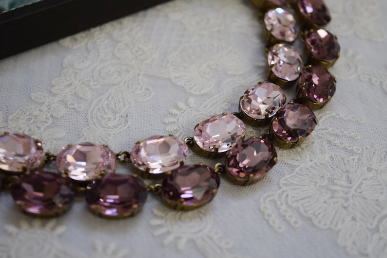 May include: A double-strand necklace with oval-shaped pink and purple rhinestones. The necklace is made of metal and has a vintage look.