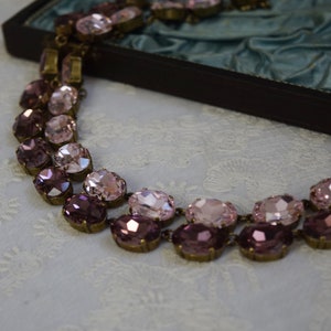 May include: A double-strand necklace with oval-shaped pink and purple glass stones set in antique gold-toned metal.