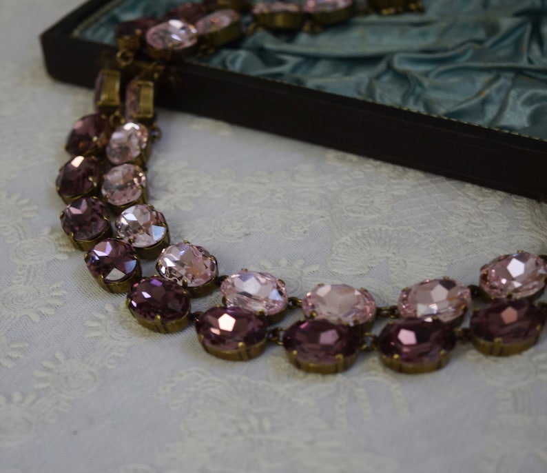 May include: A double-strand necklace with oval-shaped pink and purple glass stones set in antique gold-toned metal.