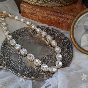 Puede incluir: Un collar que presenta una serie de cristales transparentes de forma ovalada y tallados, engastados en garras de metal dorado. Las piedras est&aacute;n unidas en una fila continua, creando un dise&ntilde;o de cadena flexible que refleja la luz.