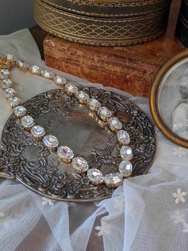 Puede incluir: Un collar que presenta una serie de cristales transparentes de forma ovalada y tallados, engastados en garras de metal dorado. Las piedras est&aacute;n unidas en una fila continua, creando un dise&ntilde;o de cadena flexible que refleja la luz.