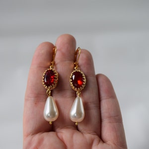 May include: Gold earrings with a red gemstone and a white pearl drop.