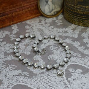 May include: A silver necklace with a teardrop-shaped crystal pendant and a row of clear crystal beads.