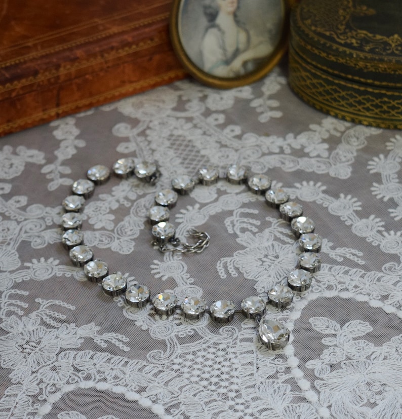 May include: A silver necklace with a teardrop-shaped crystal pendant and a row of clear crystal beads.