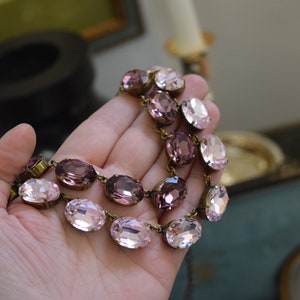 May include: A double-strand necklace with oval-shaped pink and purple crystals connected by gold-toned metal links.