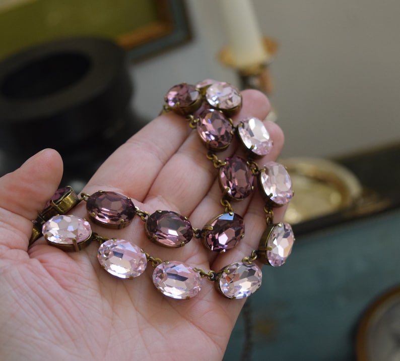 May include: A double-strand necklace with oval-shaped pink and purple crystals connected by gold-toned metal links.