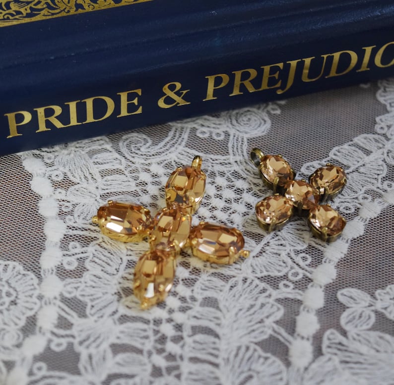 May include: Two gold-toned cross-shaped pendants with clear, faceted, amber-colored crystals. The pendants are on a white lace background.