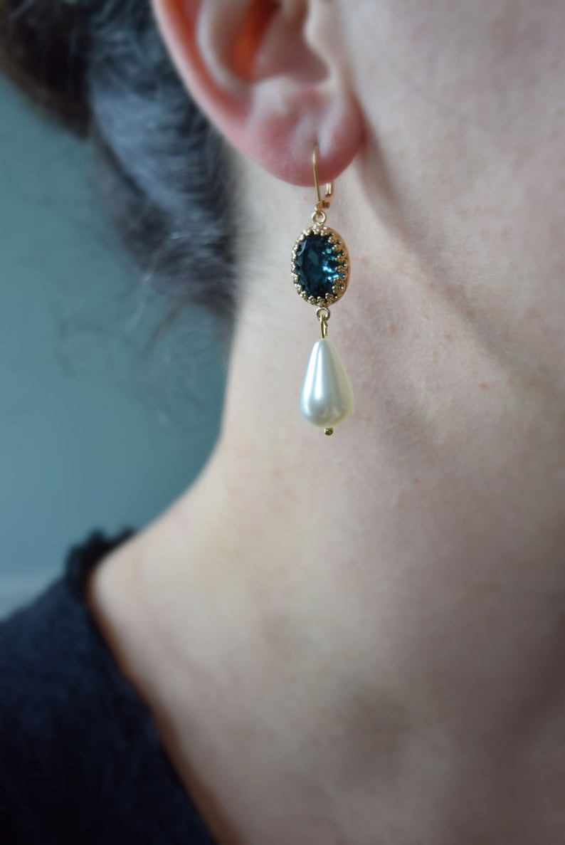 May include: Gold dangle earrings featuring a dark blue oval-shaped gemstone and a white pearl drop.