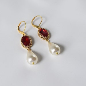 May include: Gold earrings with a red gemstone and a white pearl drop.