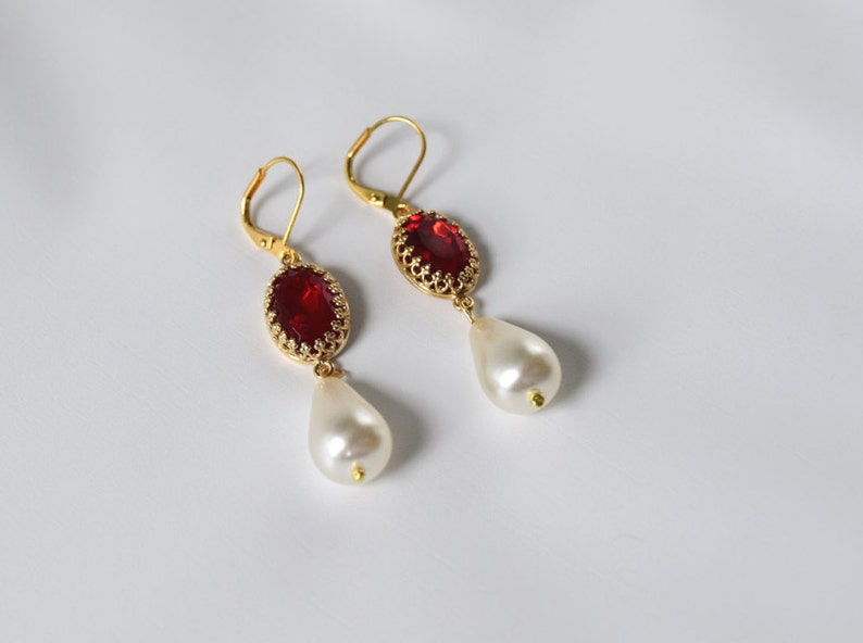 May include: Gold earrings with a red gemstone and a white pearl drop.