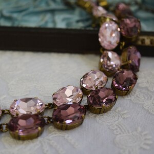 May include: A delicate necklace with a double row of oval-shaped pink and purple rhinestones set in antique gold-toned metal.