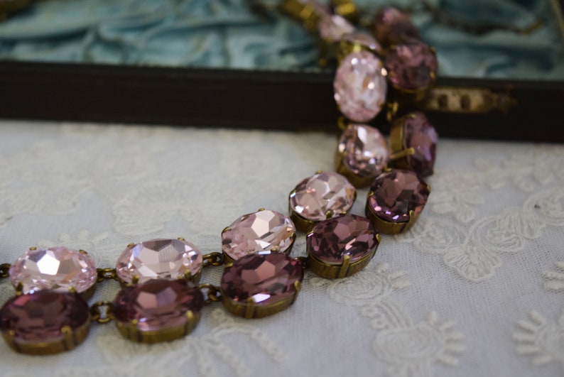 May include: A delicate necklace with a double row of oval-shaped pink and purple rhinestones set in antique gold-toned metal.