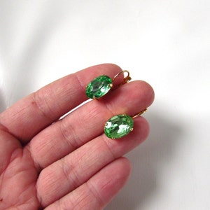 May include: A pair of green oval-shaped earrings with gold-toned metal settings. The earrings are dangle style with a hook closure.