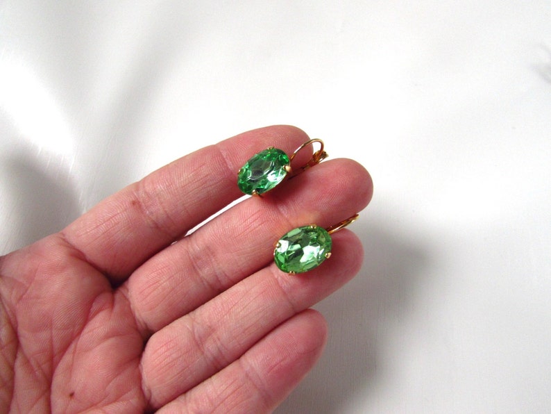 May include: A pair of green oval-shaped earrings with gold-toned metal settings. The earrings are dangle style with a hook closure.
