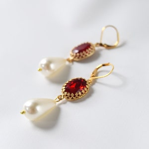 May include: A pair of gold earrings with red gemstone and white pearl accents. The earrings have a delicate, ornate design.