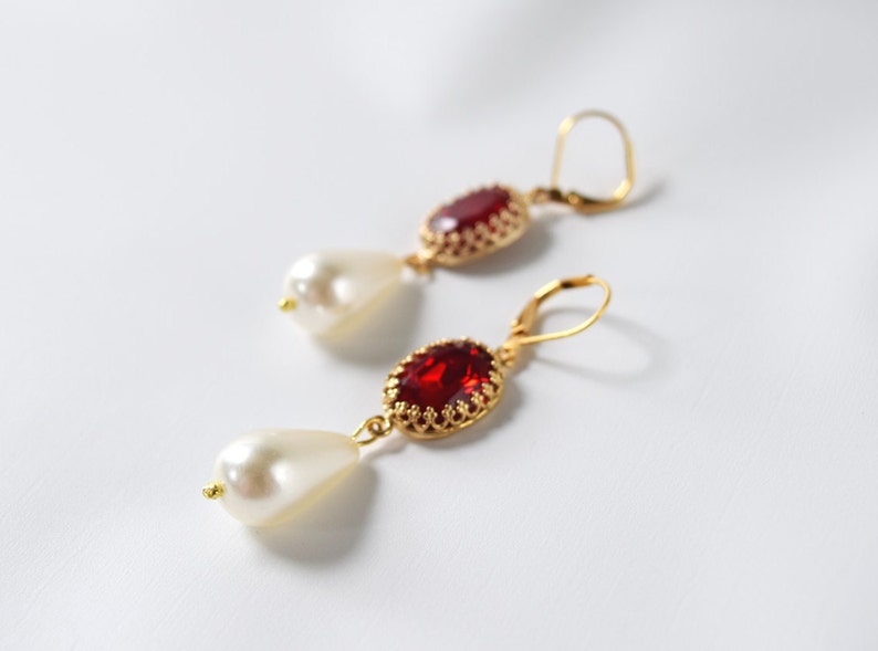 May include: A pair of gold earrings with red gemstone and white pearl accents. The earrings have a delicate, ornate design.