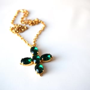 May include: A gold chain necklace with a pendant featuring a green crystal cross.