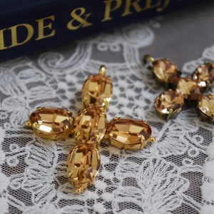 May include: Two gold-tone cross-shaped charms with amber-colored crystal accents. The charms are on a white lace background.