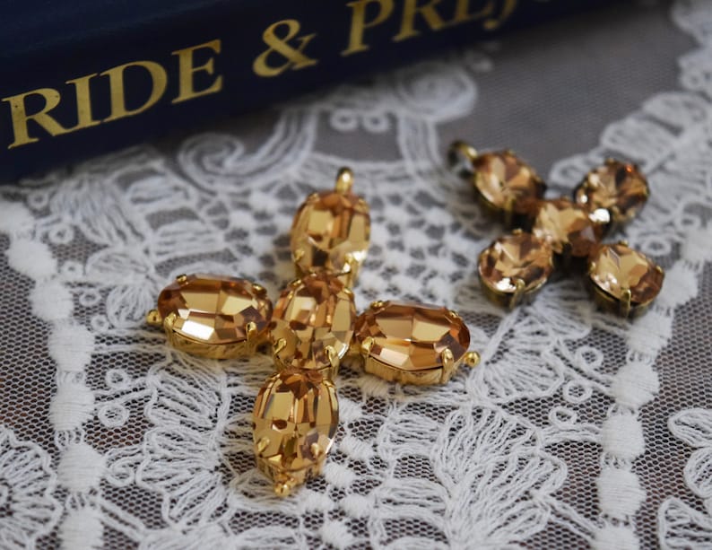 May include: Two gold-tone cross-shaped charms with amber-colored crystal accents. The charms are on a white lace background.