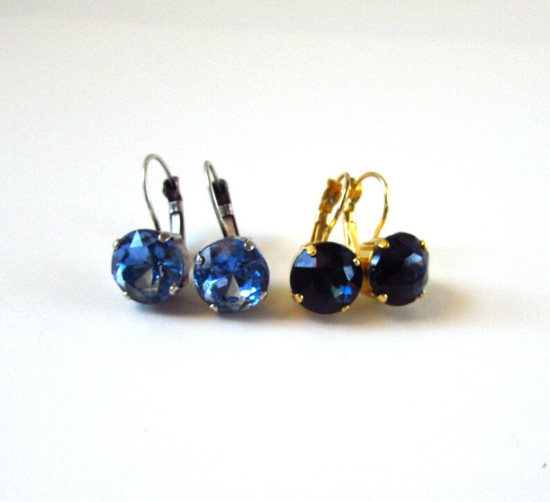 May include: Two pairs of earrings with blue gemstones. One pair has silver ear wires and a light blue gemstone. The other pair has gold ear wires and a dark blue gemstone.
