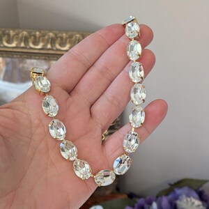 Puede incluir: Un collar de tono dorado que presenta una serie de cristales transparentes de forma ovalada y facetados. Cada cristal est&aacute; montado en un engaste de metal dorado, creando una cadena continua de piedras brillantes que descansa en la palma.