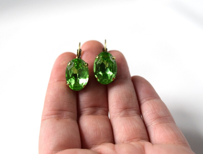 May include: A pair of green oval-shaped earrings with gold-toned metal settings.