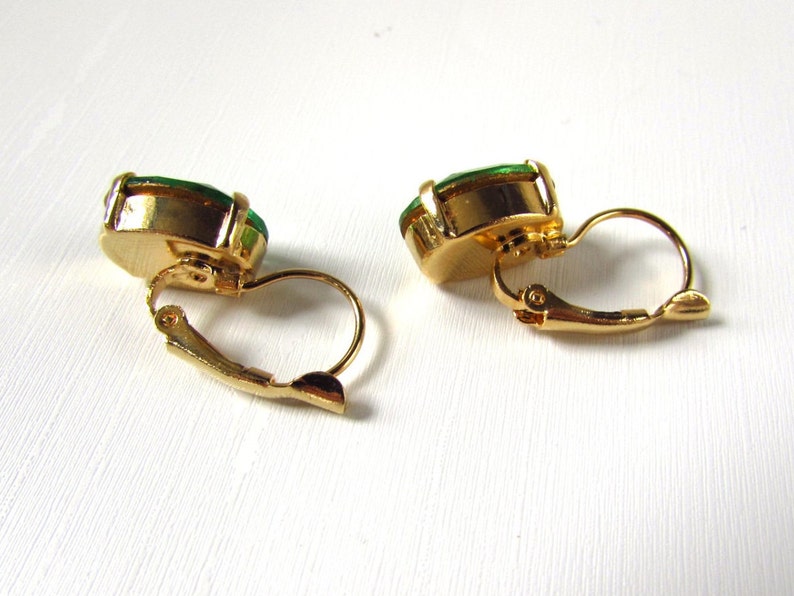 May include: A pair of gold tone clip-on earrings with green oval-shaped stones.
