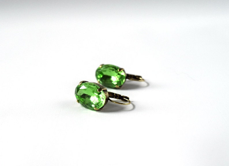 May include: A pair of green oval-shaped earrings with gold-toned metal settings.
