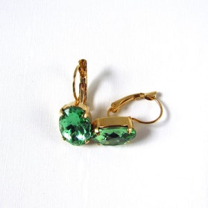 May include: A pair of gold earrings with green oval-shaped gemstones. The earrings have a lever back closure.