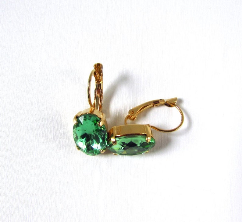 May include: A pair of gold earrings with green oval-shaped gemstones. The earrings have a lever back closure.