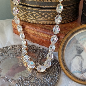 Puede incluir: Un collar que presenta una hilera continua de cristales transparentes de forma ovalada y tallados, montados en engastes de metal dorado. Los cristales est&aacute;n unidos entre s&iacute; formando una cadena flexible que refleja la luz en sus superficies.