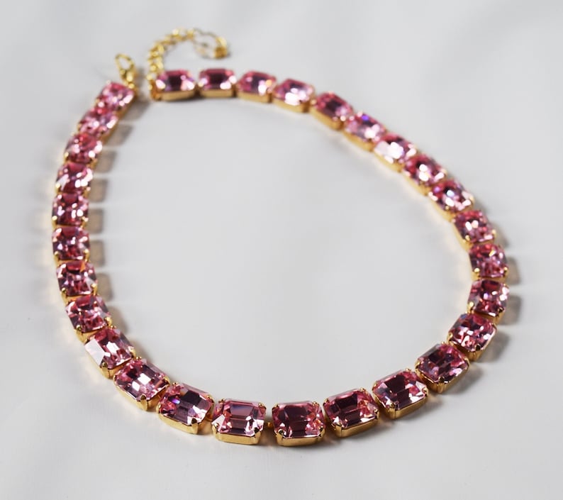 May include: A pink crystal necklace with a gold chain and rectangular-shaped crystals.