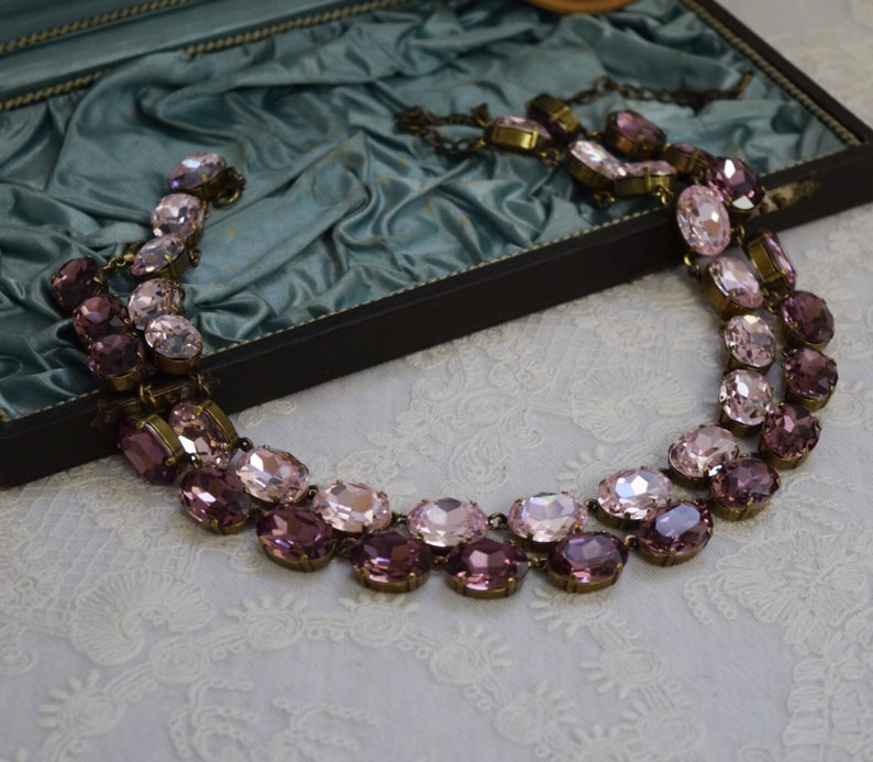 May include: A two-strand necklace with oval-shaped pink and purple crystals. The necklace is made of metal and has a vintage look.