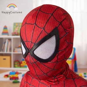 May include: A red fabric mask featuring a black spiderweb pattern across the surface. The mask includes two large, angular eye openings framed in black with white mesh lenses. The design covers the head and neck area completely.