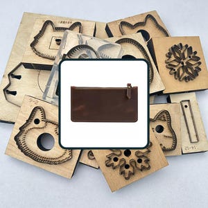 May include: A brown leather wallet with a zipper closure is displayed against a backdrop of various wooden craft dies. The dies feature cut-out shapes, including a cat, a snowflake, and other geometric designs. The wallet is rectangular and appears to be new.