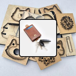 May include: A brown leather key holder with a snap closure, holding keys and a car remote. The key holder is surrounded by various wooden die-cut shapes, including animal and snowflake designs, used for crafting.
