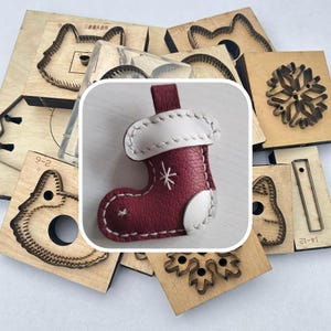 May include: A Christmas stocking keychain in burgundy leather with white accents and a snowflake design. The keychain is surrounded by wooden craft dies in various shapes, including a cat, a snowflake, and other festive designs.
