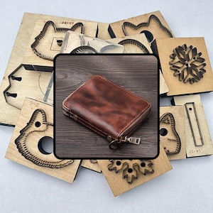 Puede incluir: Una cartera de cuero marrón con cierre de cremallera se muestra sobre una superficie de madera, rodeada de varias formas troqueladas de madera. Las formas troqueladas incluyen caras de animales, copos de nieve y otros diseños decorativos.