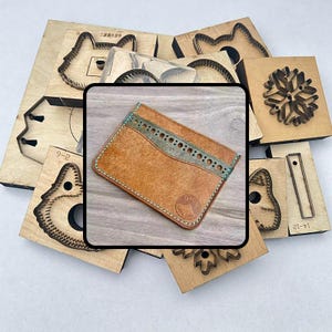 May include: A handcrafted brown leather cardholder with a teal accent and stitching. The cardholder is surrounded by various wooden die-cut shapes, including animal profiles and a snowflake design. The leather has a natural, textured appearance.
