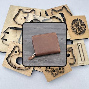 以下が含まれることがあります： 茶色の革製財布が写っています。ファスナー開閉式で、周囲には動物の顔や雪の結晶のデザインなど、さまざまな木製の型抜きが配置されています。財布は長方形で、新品のようです。