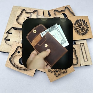 May include: A brown leather wallet with a snap closure, open to reveal cash. The wallet is surrounded by wooden craft tools with various cut-out shapes, including a snowflake and animal figures. The wallet is held in a hand.