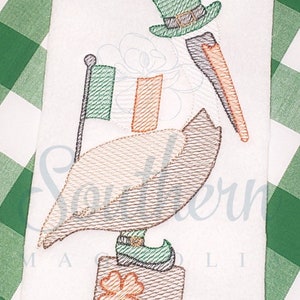 May include: Embroidered design of a pelican wearing a green leprechaun hat and holding an Irish flag. The pelican is standing on a block with a four-leaf clover.