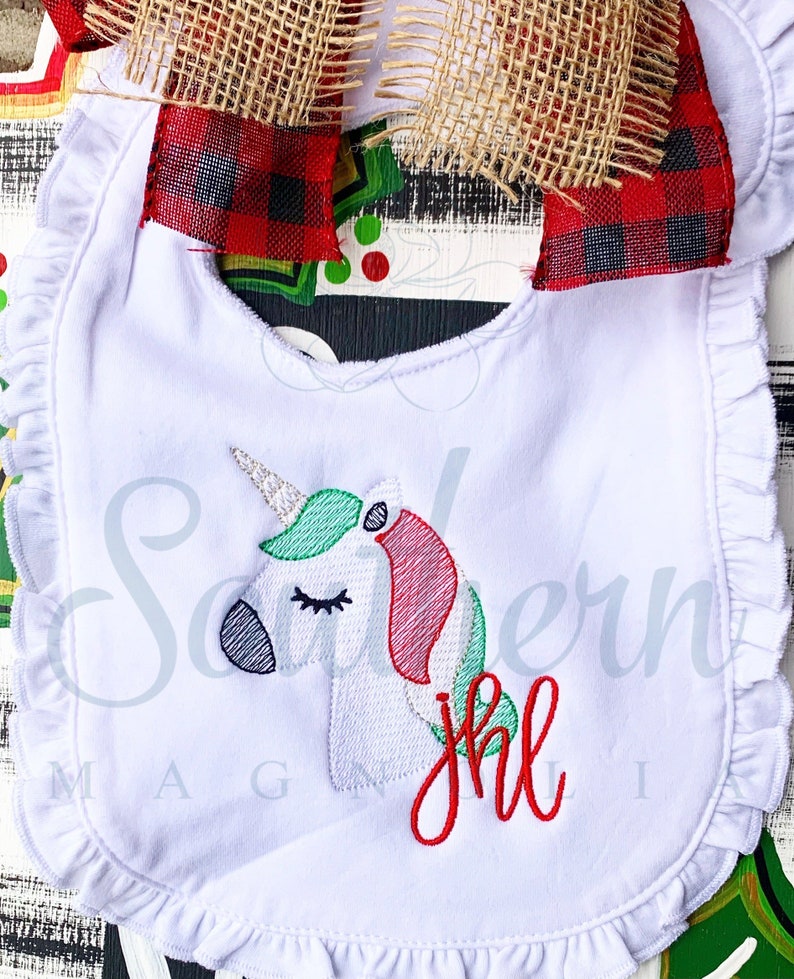 May include: White baby bib with a green and red embroidered unicorn and the word "Jingle" in red embroidery.