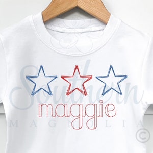 May include: White t-shirt with three embroidered stars, two blue and one red, and the name "maggie" embroidered in red.
