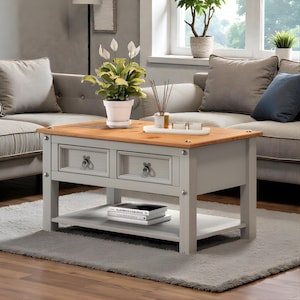 May include: A grey and wood coffee table with two drawers and a lower shelf. The table has a light grey base and a natural wood top. A potted plant and decorative items sit on top of the table.