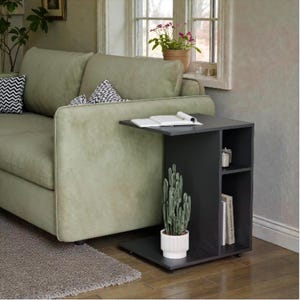 May include: A black side table with a built-in shelf and a tabletop that extends over the side of a green sofa. A potted cactus and books are on the table. The table is 61 cm high, 41 cm wide, and 30 cm deep.