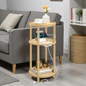 May include: A three-tiered, light-coloured bamboo side table with a round top and shelves. The top shelf holds a vase with flowers and a teacup. The middle shelf has a phone charging station. The bottom shelf has a tray with candles and books. The table is 61 cm tall.